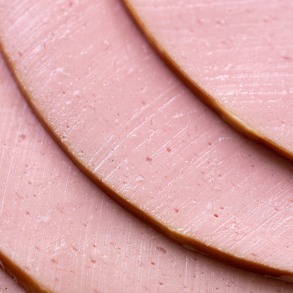 Rebanadas de mortadela jamonada servidas en tabla con pan y hierbas