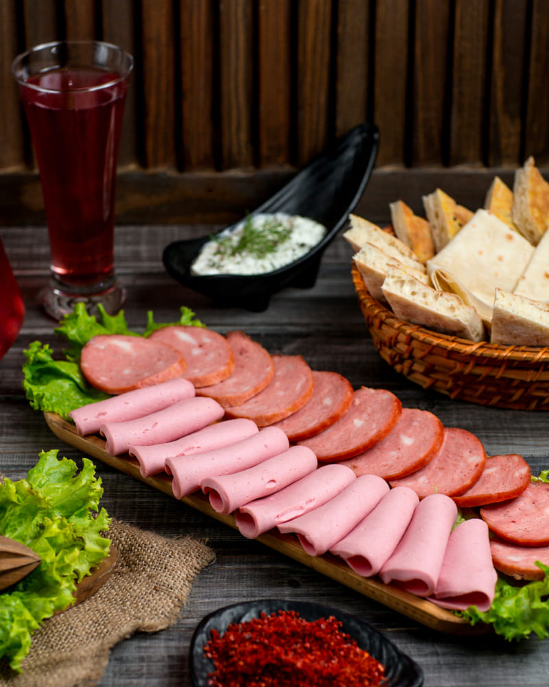 Rebanadas de mortadela jamonada servidas en tabla con pan y hierbas